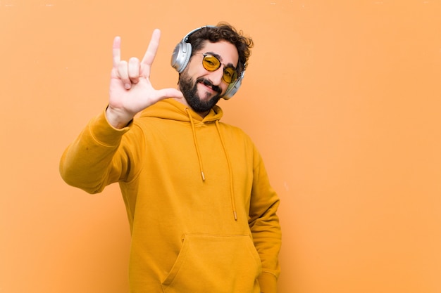 Jeune homme cool fou, écouter de la musique avec des écouteurs contre le mur orange