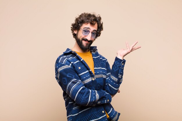 Jeune homme cool fou souriant fièrement et en toute confiance, se sentant heureux et satisfait et montrant un concept sur copie espace contre mur plat