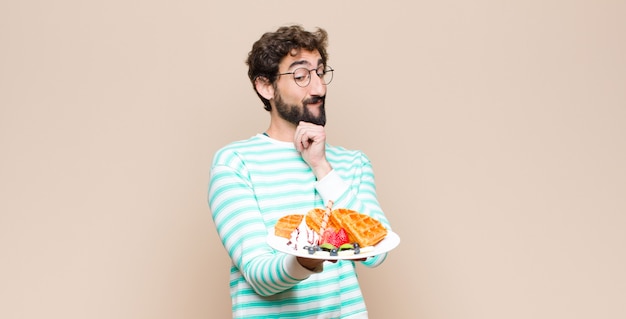 Jeune homme cool avec des gaufres contre un mur plat.