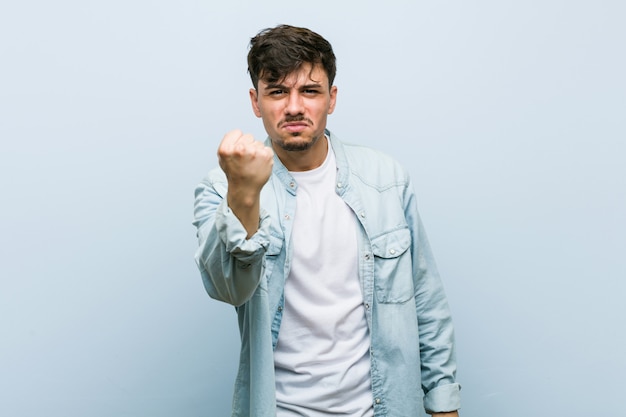 Jeune homme cool hispanique montrant le poing avec une expression faciale agressive.