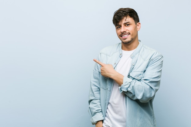 Jeune homme cool hispanique souriant et pointant de côté, montrant quelque chose à l'espace vide.