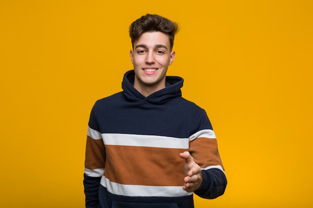 Jeune homme cool portant un sweat à capuche qui s'étend de la main à la caméra dans le geste de salutation.