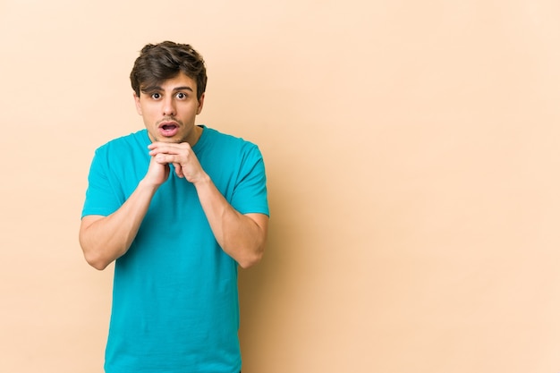 Jeune homme cool priant pour la chance, étonné et ouvrant la bouche à l'avant.