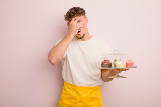 Jeune homme cool qui a l'air choqué, effrayé ou terrifié, couvrant le visage avec le concept de gâteaux faits maison à la main