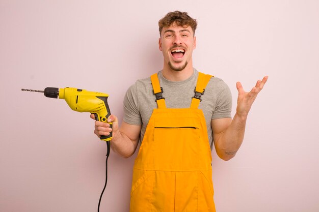 Jeune homme cool se sentant heureux et étonné de quelque chose d'incroyable concept de bricoleur et de forage