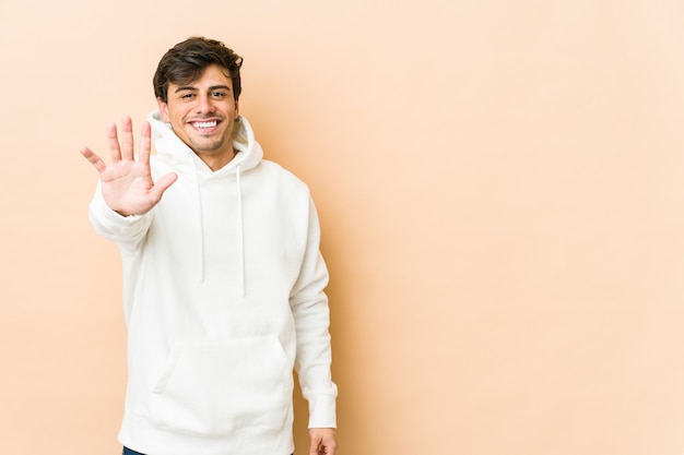 Jeune homme cool souriant gai montrant le numéro cinq avec les doigts.