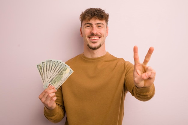 Jeune homme cool souriant et sympathique montrant le concept de billets de banque numéro deux en dollars