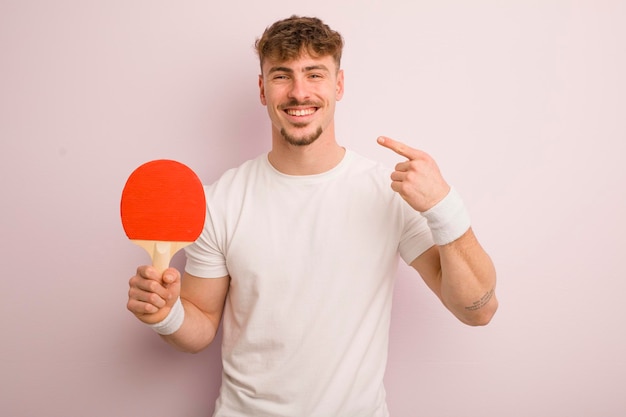 Jeune homme cool souriant en toute confiance pointant vers son propre concept de ping-pong au large sourire