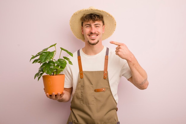 Jeune homme cool souriant en toute confiance pointant vers son propre jardinier et plante au large sourire