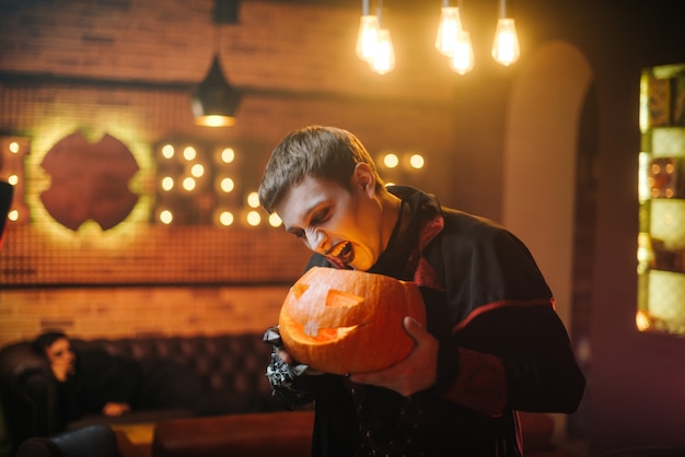 Jeune homme en costume d'halloween du comte dracula tient une citrouille festive sculptée