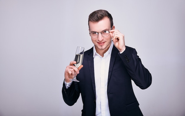 Jeune homme en costume tenant ses lunettes et un verre de champagne isolé sur fond gris