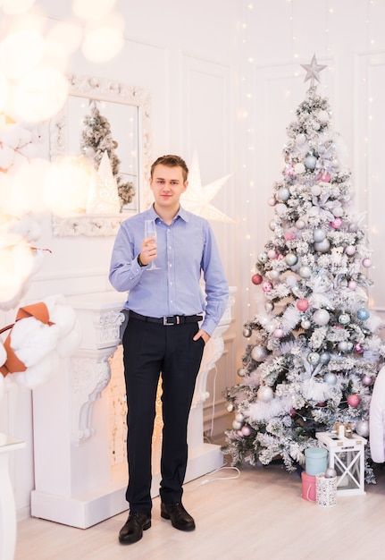 Jeune homme à côté de l'arbre de Noël avec une coupe de champagne dans ses mains