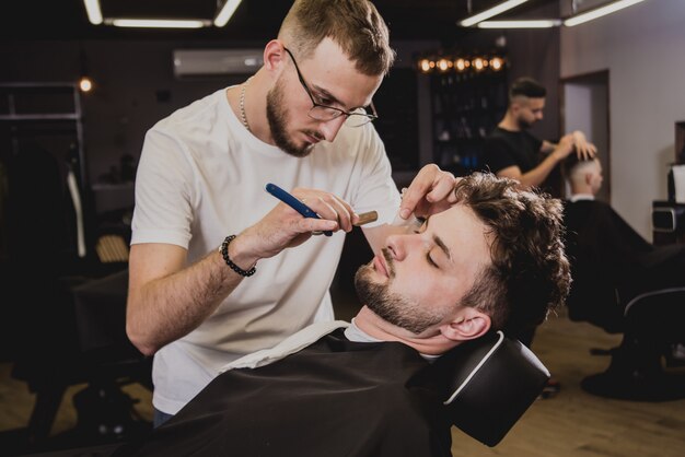 Jeune homme avec coupe de cheveux tendance au salon de coiffure. Barber fait la coiffure et la coupe de la barbe.