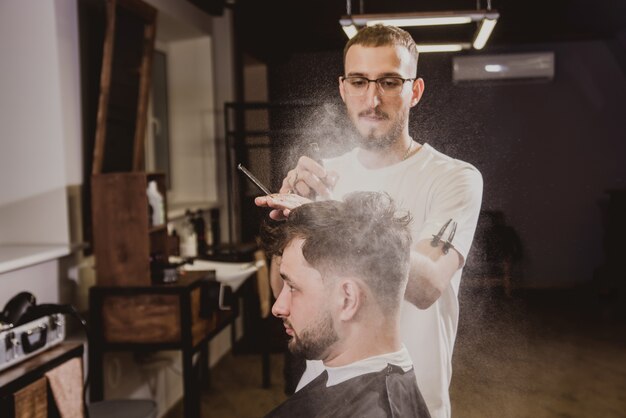 Jeune homme avec coupe de cheveux tendance au salon de coiffure. Barber fait la coiffure et la coupe de la barbe.