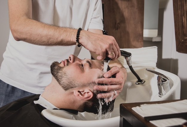 Jeune homme avec coupe de cheveux tendance au salon de coiffure. Barber lave la tête du client.