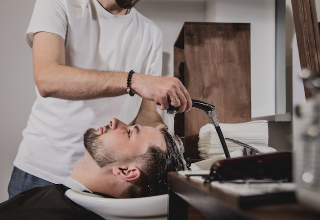 Jeune homme avec coupe de cheveux tendance au salon de coiffure. Barber lave la tête du client.