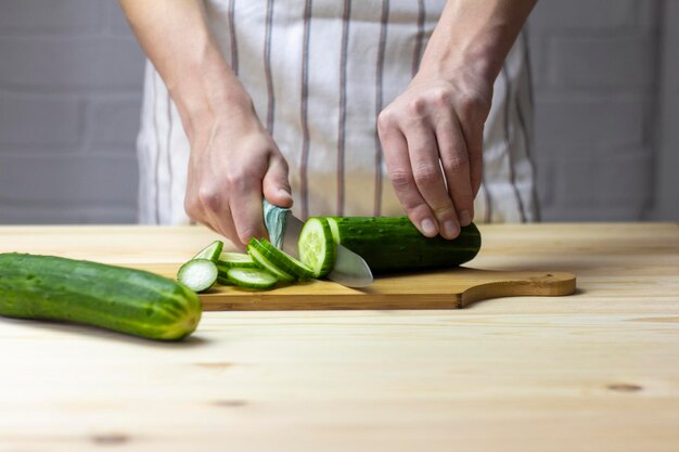 Un jeune homme coupe soigneusement un concombre avec un couteau sur une planche à découper.