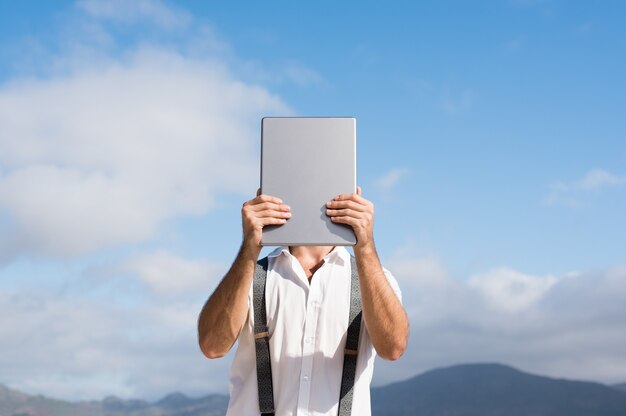 Jeune homme couvrant le visage avec tablette numérique