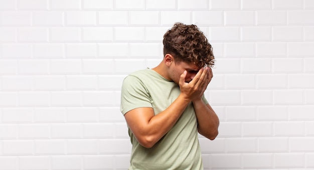 Jeune homme couvrant les yeux avec les mains avec un regard triste et frustré de désespoir