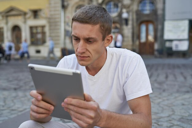 Jeune homme créatif assis sur le trottoir et utilisant une tablette