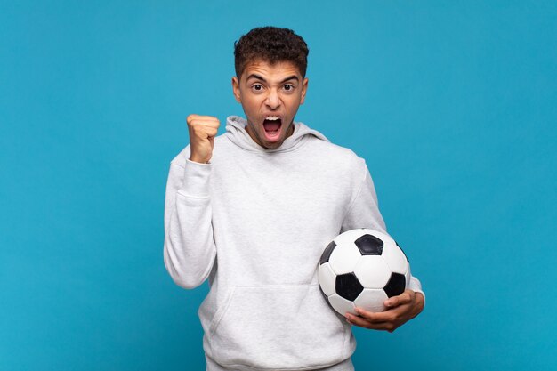 Jeune homme criant agressivement avec une expression de colère ou les poings serrés célébrant le succès. concept de football