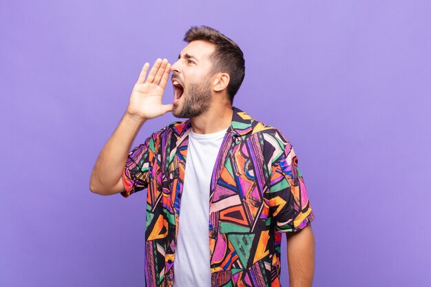 Jeune homme criant fort et en colère pour copier l'espace sur le côté, avec la main à côté de la bouche