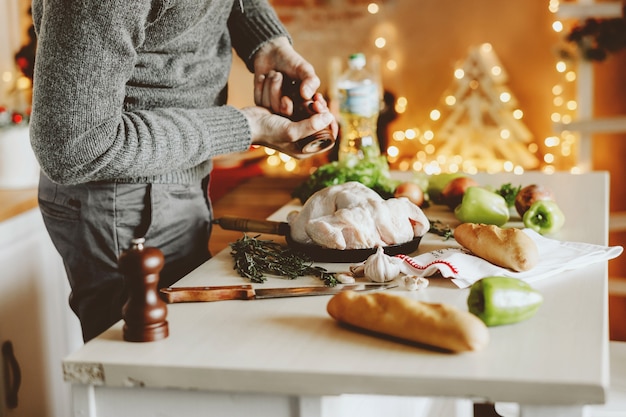 Jeune homme cuire du poulet cru pour Noël.