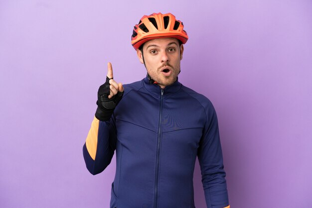 Jeune homme cycliste brésilien isolé sur fond violet dans l'intention de réaliser la solution tout en levant un doigt vers le haut