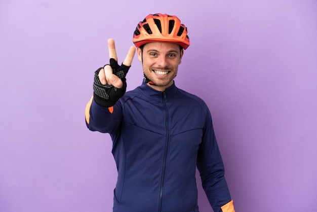 Jeune homme cycliste brésilien isolé sur fond violet souriant et montrant le signe de la victoire