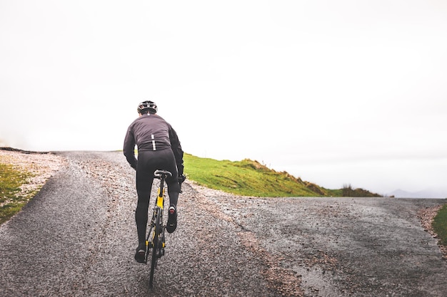 Jeune homme cycliste caucasien atteignant le sommet de la colline d'une route goudronnée.