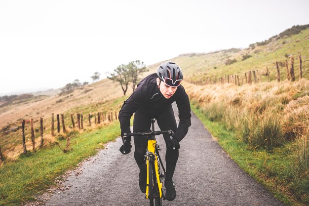 Jeune homme cycliste caucasien sprintant en montant une colline dans une montagne brumeuse.