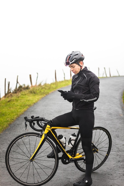 Jeune homme cycliste caucasien utilisant un smartphone sur son vélo au sommet d'une montagne.