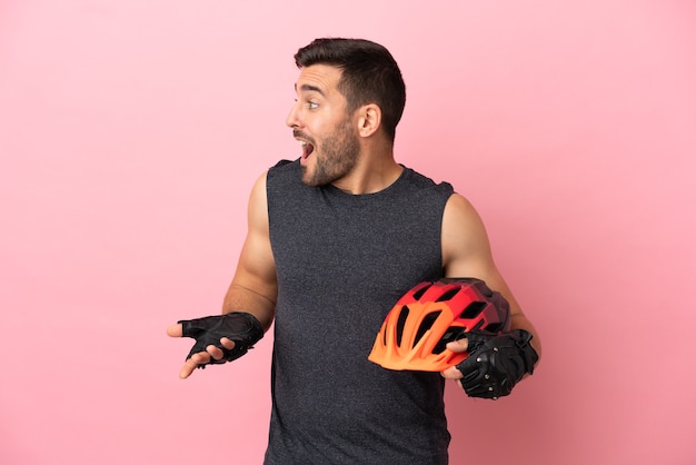 Jeune homme cycliste isolé sur fond rose avec une expression de surprise tout en regardant de côté