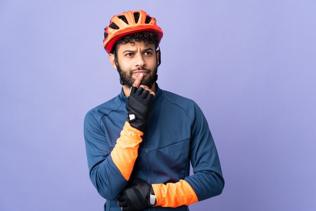 Jeune homme cycliste marocain isolé sur mur violet ayant des doutes tout en regardant vers le haut