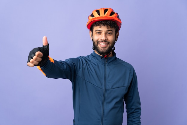 Jeune homme cycliste marocain isolé sur mur violet donnant un geste de pouce en l'air