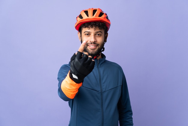 Jeune homme cycliste marocain isolé sur mur violet faisant le geste à venir