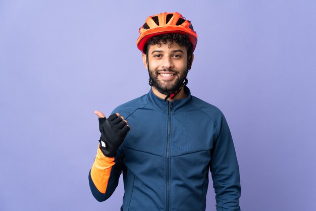 Jeune homme cycliste marocain isolé sur violet pointant vers le côté pour présenter un produit