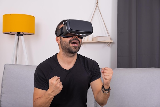 Jeune homme dans un casque de lunettes vr à la maison sur un canapé excité faisant des gestes vidéo sur l'éducation à la technologie future ...