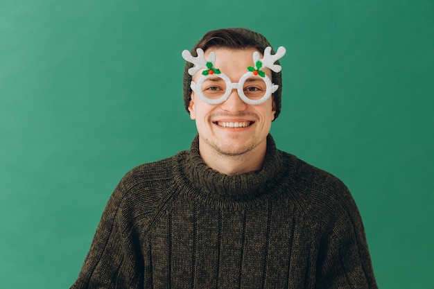 Un jeune homme dans un chandail chaud, une casquette et des lunettes de carnaval isolés sur fond vert