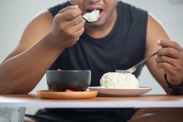 Un jeune homme dans un débardeur noir est assis joyeusement à la maison pour le déjeunerSe concentre sur une assiette de riz en gros plan