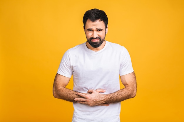 Jeune homme dans la douleur tenant son estomac blessé isolé sur fond jaune. Douleur abdominale.