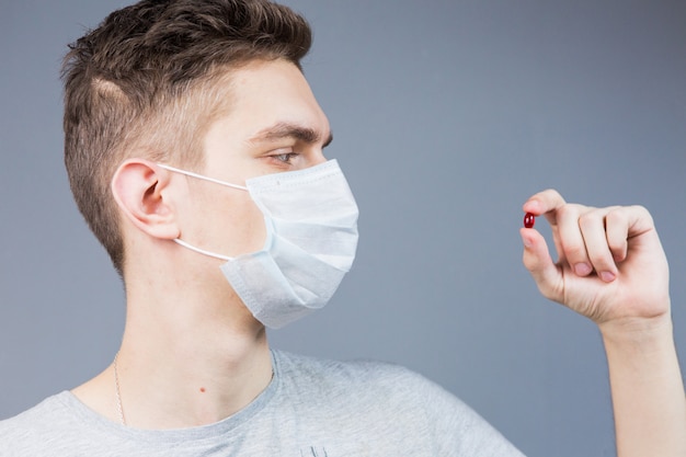 Jeune homme dans un masque avec une pilule rouge à la main