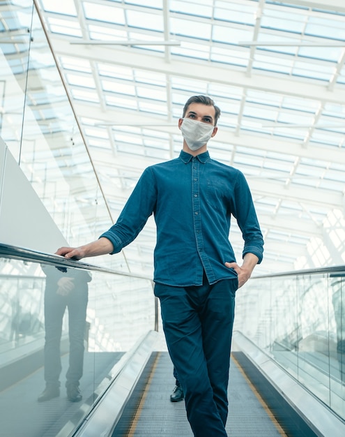 Jeune homme dans un masque de protection debout sur les marches de l'escalator