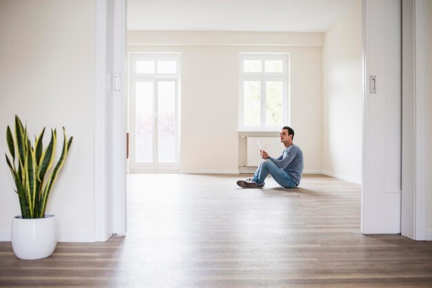 Jeune homme dans une nouvelle maison assis sur le sol avec tablette
