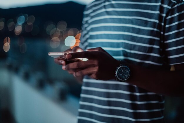 Le jeune homme dans une rue urbaine la nuit envoyant des SMS sur un smartphone avec bokeh et lumières de la ville au néon en arrière-plan. Photo de haute qualité. Photo de haute qualité