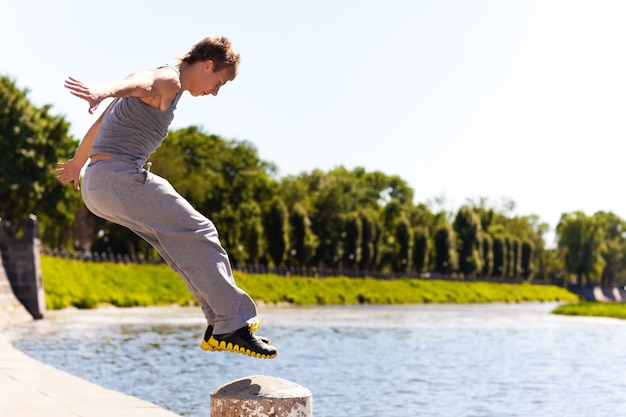 Jeune homme, dans, sportswear, sauter, et, pratiquer, parkour, dehors, sur, barrière pierre, sur, rivière, remblai, sur, clair, jour été