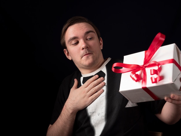 Un jeune homme dans un t-shirt noir tenez avec surprise un cadeau sur un noir