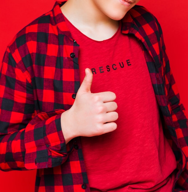 Jeune homme dans un t-shirt rouge et une chemise à carreaux sur fond rouge montre le super signe. Photo verticale