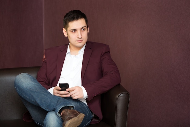 Jeune homme dans une veste rouge avec un téléphone à la main.