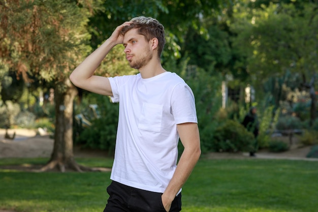 Jeune homme debout dans le parc et tenant sa main sur sa tête